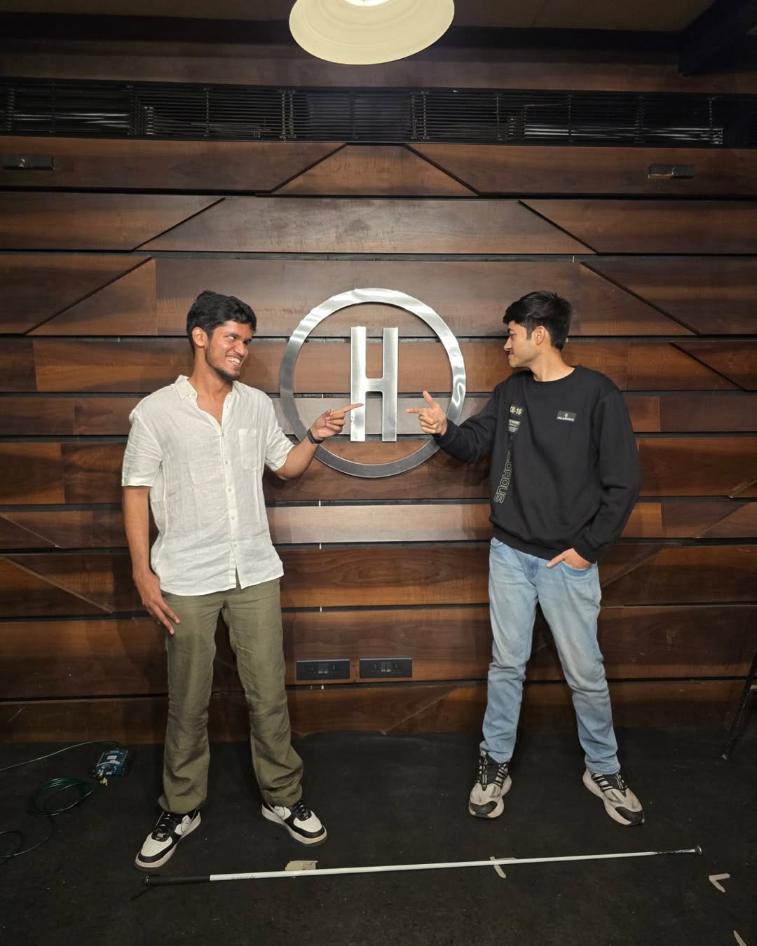 Bhavya and Kushal, standing on a carpeted stage, point at the H from the iconic Habitat logo